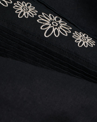 A close-up of a soft black Brisa Linen Shirt - Onyx by Dandy Del Mar with embroidered white flowers.