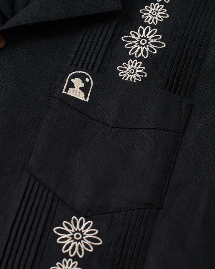 A black Brisa Linen Shirt in Onyx color by Dandy Del Mar with embroidered floral pocket.