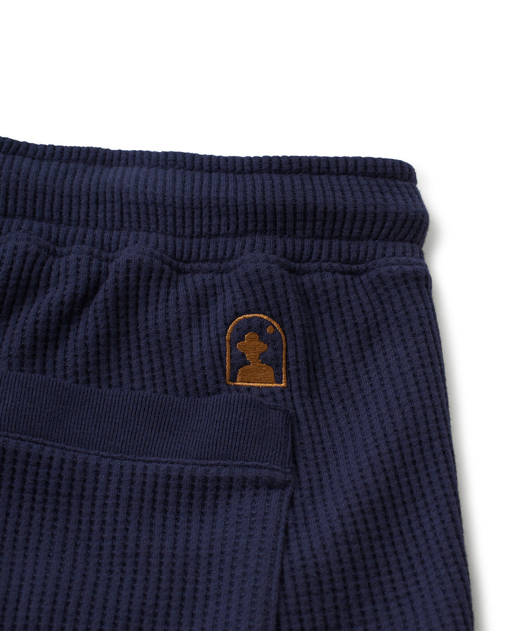 The pocket of a Dandy Del Mar Cannes Short - Luxe Navy with a brown logo.
