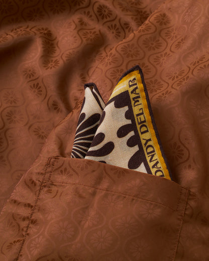 A Corsica Corduroy Jacket in Sangria, featuring a brown floral-patterned design, boasts a patterned pocket square with "Dandy Del Mar" text, elegantly inserted in the chest pocket.