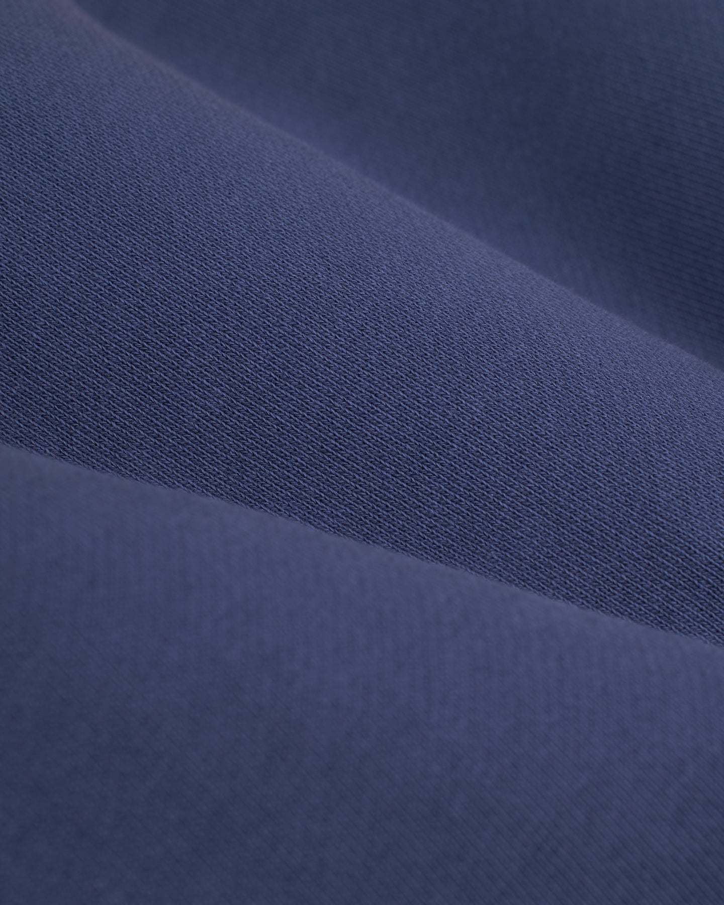 Close-up of the Moontide French terry fabric from Dandy Del Mar's The Marseille French Terry Short, showcasing a dark blue hue with a smooth, slightly textured surface. The fabric appears to be folded, creating soft, wavy contours reminiscent of an elastic waist drawstring trainer.