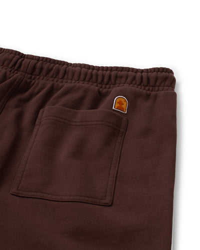 Close-up of The Marseille French Terry Shorts - Carajillo by Dandy Del Mar, featuring a brown elastic waistband, single back pocket, and a small orange logo patch above the pocket.