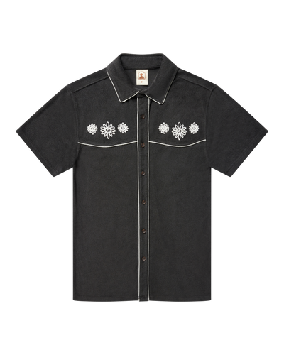 The Gaucho Terry Cloth Shirt - Onyx by Dandy Del Mar is a short-sleeve black shirt with white floral chest embroidery and contrasting white piping on the collar and yoke.