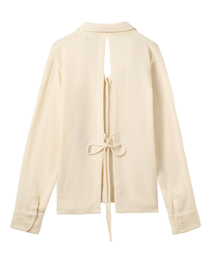 The Sevilla Top - Scallop by Dandy Del Mar: a cream long-sleeve shirt with a back slit, tie waist closure, and buttoned cuffs, shown flat on a black background.