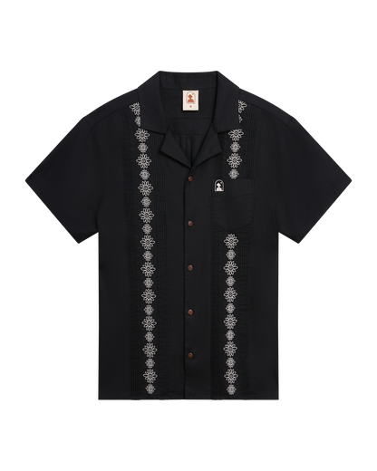The Brisa Linen Shirt - Onyx by Dandy Del Mar: a short-sleeve black linen shirt with vertical white gardenia embroidery, chest pocket, and coconut shell buttons, shown laid flat on a white background.