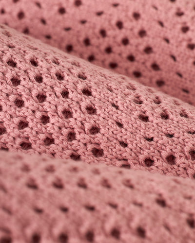 Close-up of The Antibes Crochet Polo Shirt - Dawn by Dandy Del Mar, highlighting the pink crochet knit fabric's repeating small holes and textured yarn.