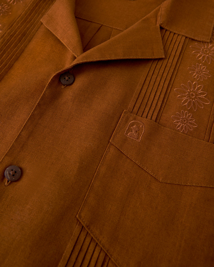 Close-up of The Brisa Linen Shirt - Sedona by Dandy Del Mar, showcasing gardenia floral embroidery and a large chest pocket, accentuated by coconut shell buttons.