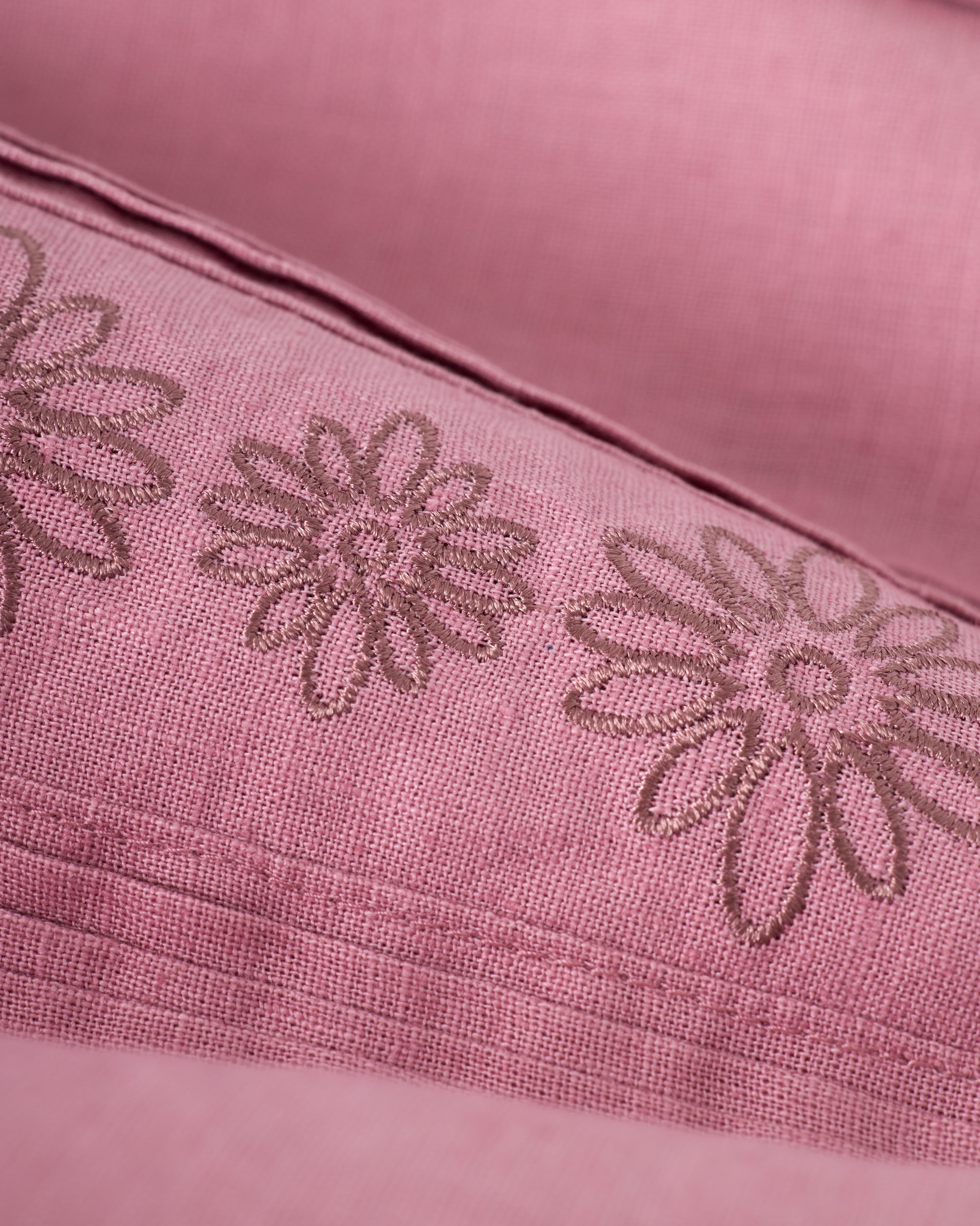 Close-up of The Brisa Linen Shirt - Dawn by Dandy Del Mar, featuring pink fabric with embroidered floral patterns and stitching details.