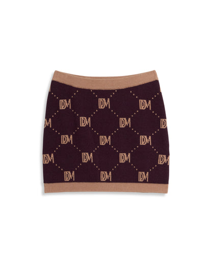 The Canela Skirt - Amethyst by Dandy Del Mar is a sweater knit mini skirt with a stylish monogram pattern in dark brown, featuring the letters "DM" and beige borders on the waist and hem.