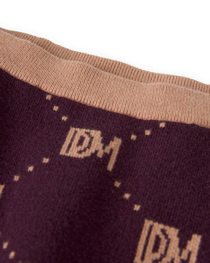 Close-up of The Canela Skirt - Amethyst by Dandy Del Mar, featuring a fabric with a monogram pattern displaying the letters "DM" in beige against a dark brown background, reminiscent of a classic sweater knit mini skirt with an elastic waistband.