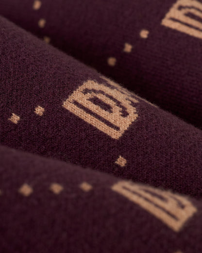 A detailed view of The Canela Skirt - Amethyst by Dandy Del Mar, highlights its maroon sweater knit fabric with an elastic waistband. The design is adorned with light brown geometric and monogram patterns interspersed with delicate dots.