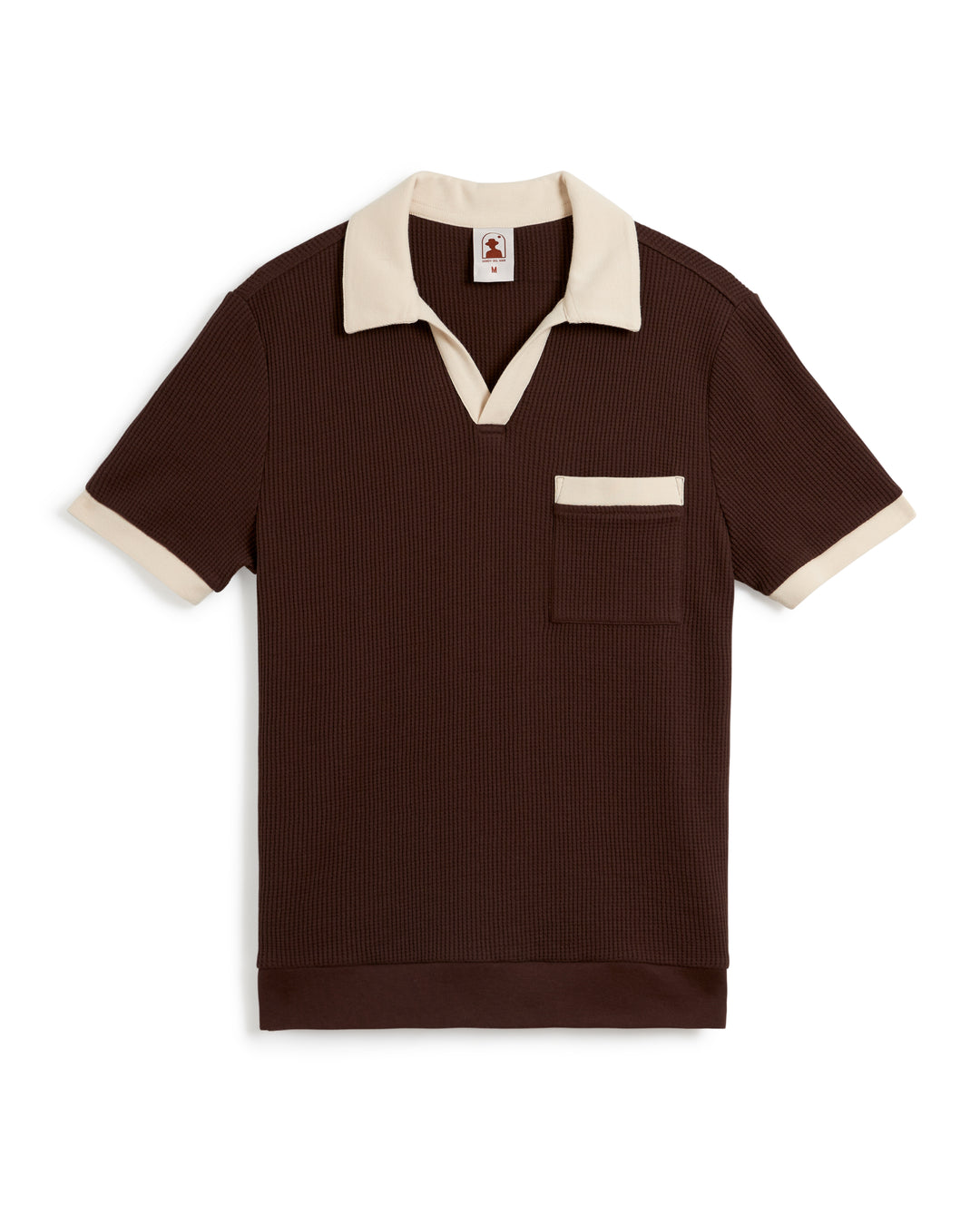 The Cannes Waffle Knit Shirt - Carajillo by Dandy Del Mar is a short-sleeved, dark brown, waffle knit fabric polo shirt featuring a beige collar and sleeve cuffs, a beige-trimmed chest pocket, and a split V-neck design.