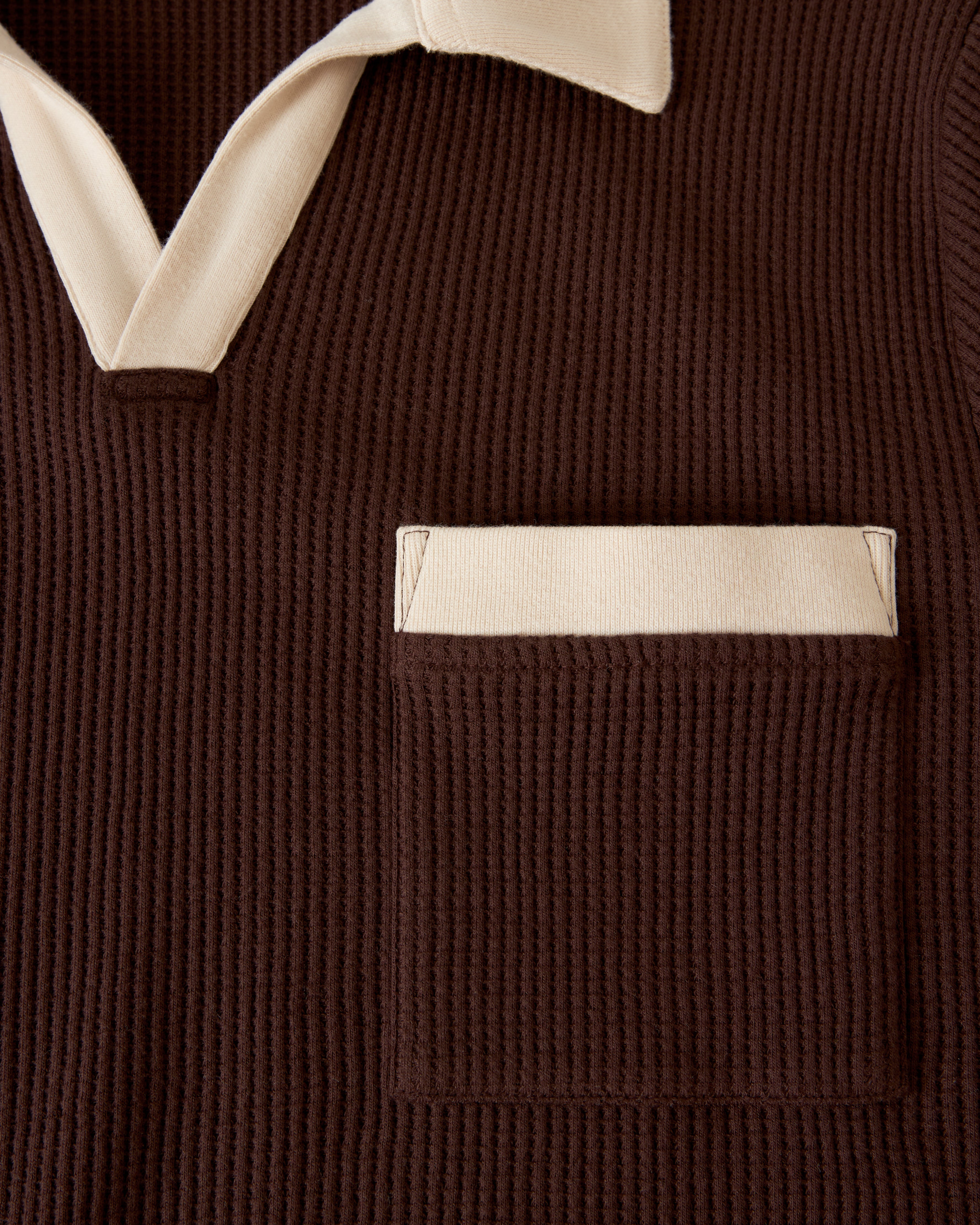 Close-up of The Cannes Waffle Knit Shirt - Carajillo by Dandy Del Mar, showcasing its brown textured fabric with a beige buttonless polo collar and a beige-trimmed pocket on the left chest.