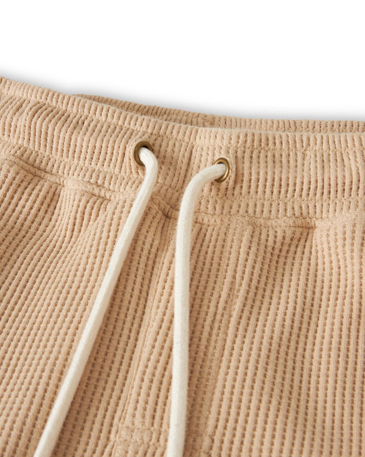 Close-up of the waistband of The Cannes Waffle Knit Shorts - Truffle by Dandy Del Mar, featuring white drawstrings threaded through metal eyelets, made from 100% cotton.