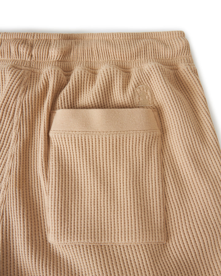 Close-up of the back pocket on a pair of "The Cannes Waffle Knit Shorts - Truffle" by Dandy Del Mar, showcasing the unique waffle texture and elastic waistband. Made from 100% cotton for comfort and durability.