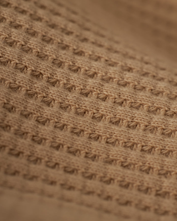 Close-up of The Cannes Waffle Knit Shorts from Dandy Del Mar in the Truffle color, featuring a light brown, 100% cotton knitted fabric with a repeating textured pattern of raised horizontal ridges and small holes, reminiscent of waffle knit fabric, creating a detailed and tactile surface.