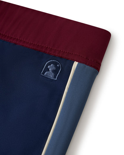 Close-up of a multicolored fabric patch on the Cassis Square Cut Swim Brief - Anchor Bordeaux by Dandy Del Mar, crafted from recycled polyester. The small logo displays a silhouette of a person in profile.