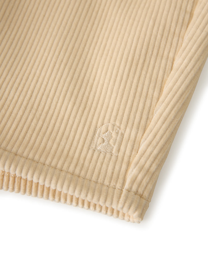 Close-up of The Corsica Corduroy Short in Scallop by Dandy Del Mar, featuring beige ribbed fabric and an embossed logo in the corner.