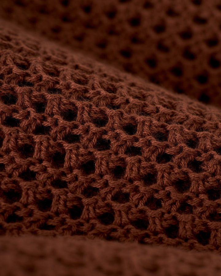 Close-up of The Dominica Crochet Tank in Cappuccino by Dandy Del Mar, showcasing its lightweight brown knitted fabric and textured open weave design reminiscent of a relaxed-fit crochet top.