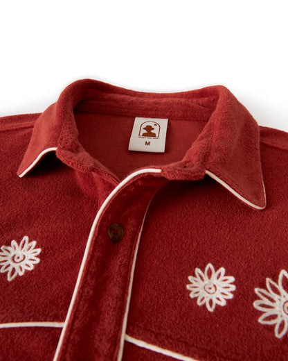 Close-up of The Gaucho Shirt - Rouge by Dandy Del Mar, featuring white embroidered flowers, white piping, and a medium size tag on the collar.