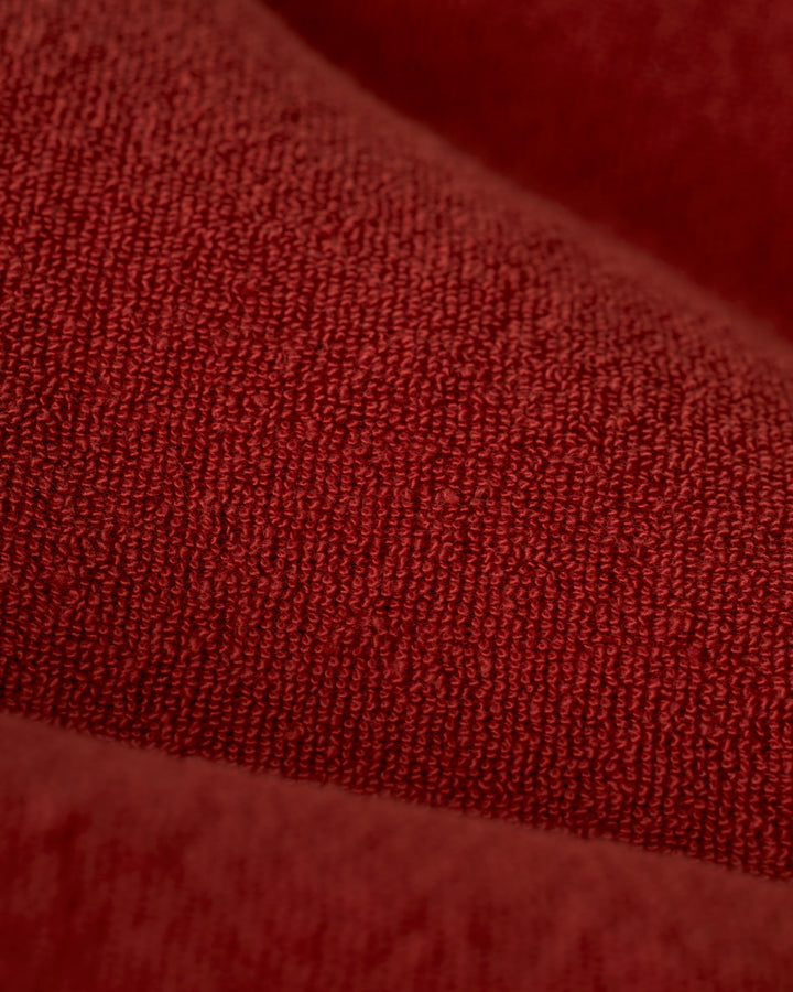 Close-up view of The Gaucho Terry Cloth Short - Rouge by Dandy Del Mar, showcasing its textured red fabric with visible stitching and a soft, woven appearance.