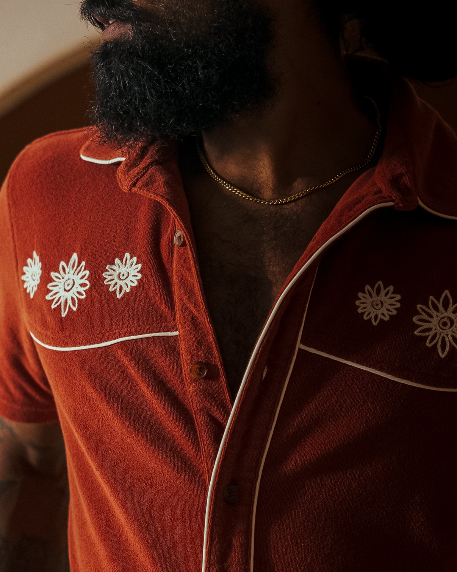 A person wearing Dandy Del Mar's Rouge Gaucho Shirt with white floral embroidery and a gold chain necklace, exuding an Equatorial Cowboy vibe.