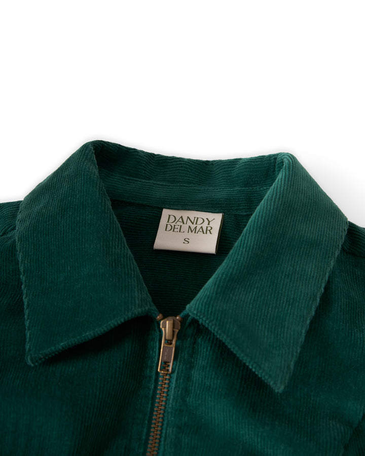 A close-up of "The Kitts Corduroy Dress - Albero" by Dandy Del Mar showcases its tailored style, green corduroy fabric with a zipper and collar, featuring a label inside that reads "Dandy Del Mar".