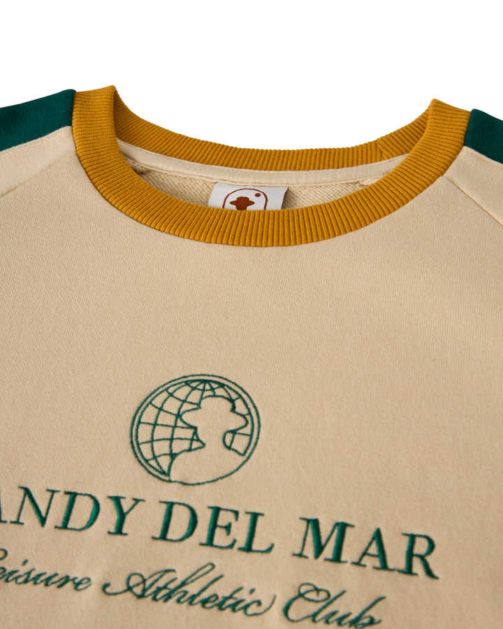 Close-up of The Marseille French Terry Pullover - Sabbia by Dandy Del Mar, showcasing green "SANDY DEL MAR" and "Leisure Athletic Club" lettering with a globe graphic. A mustard yellow collar adds a pop to this classic Raglan design.