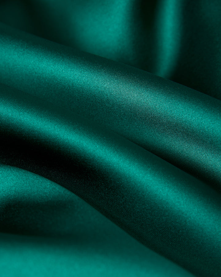 Close-up of the smooth, flowing folds of The Monaco Flounce Top - Albero by Dandy Del Mar, crafted in emerald green satin.