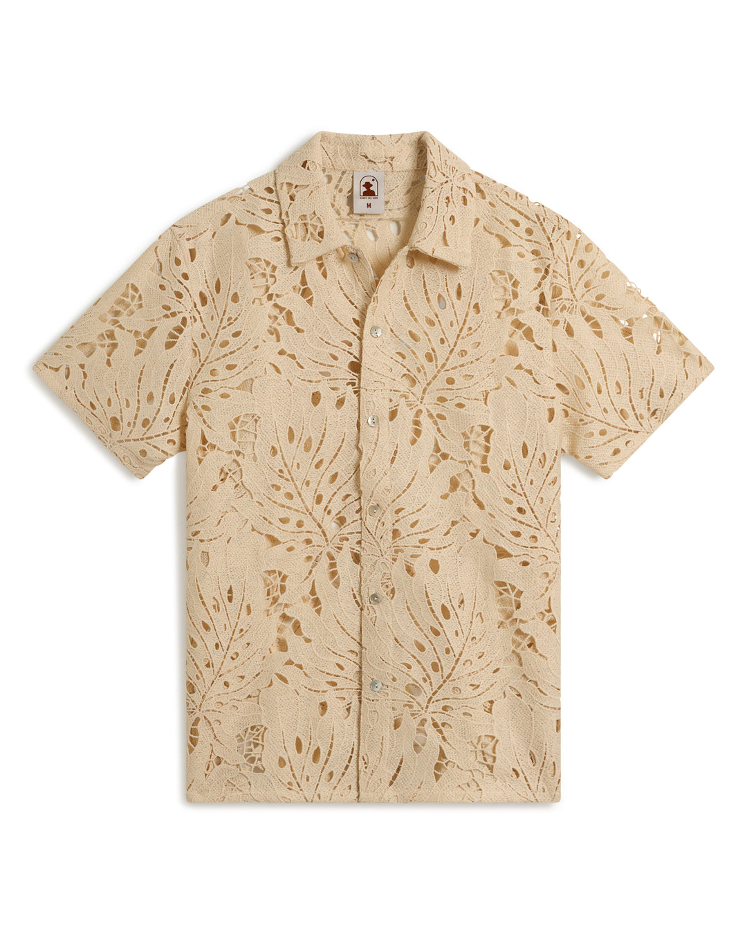 The Monstera Shirt - Scallop by Dandy Del Mar features a beige short-sleeve button-up design with a leaf and floral pattern.