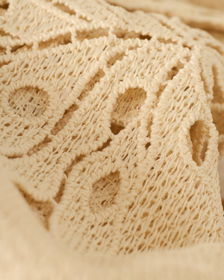 Close-up of The Monstera Shirt - Scallop by Dandy Del Mar, showcasing its beige knitted fabric with a circular pattern.