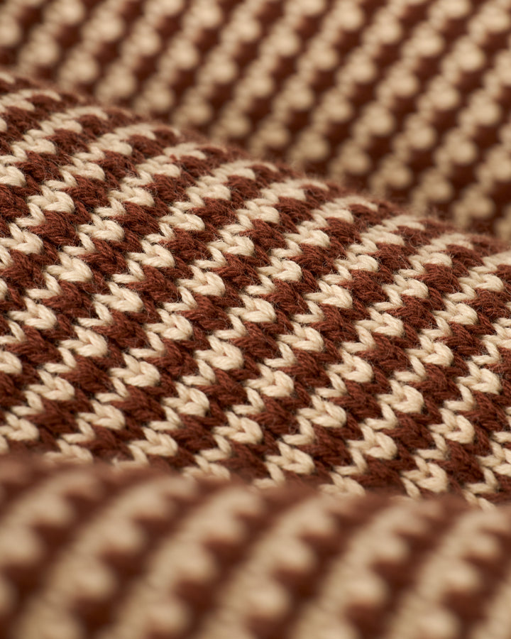 Close-up of The Palamos Knit Polo Shirt - Cappuccino by Dandy Del Mar, displaying a brown and cream striped knit pattern with rows of textured stitches.