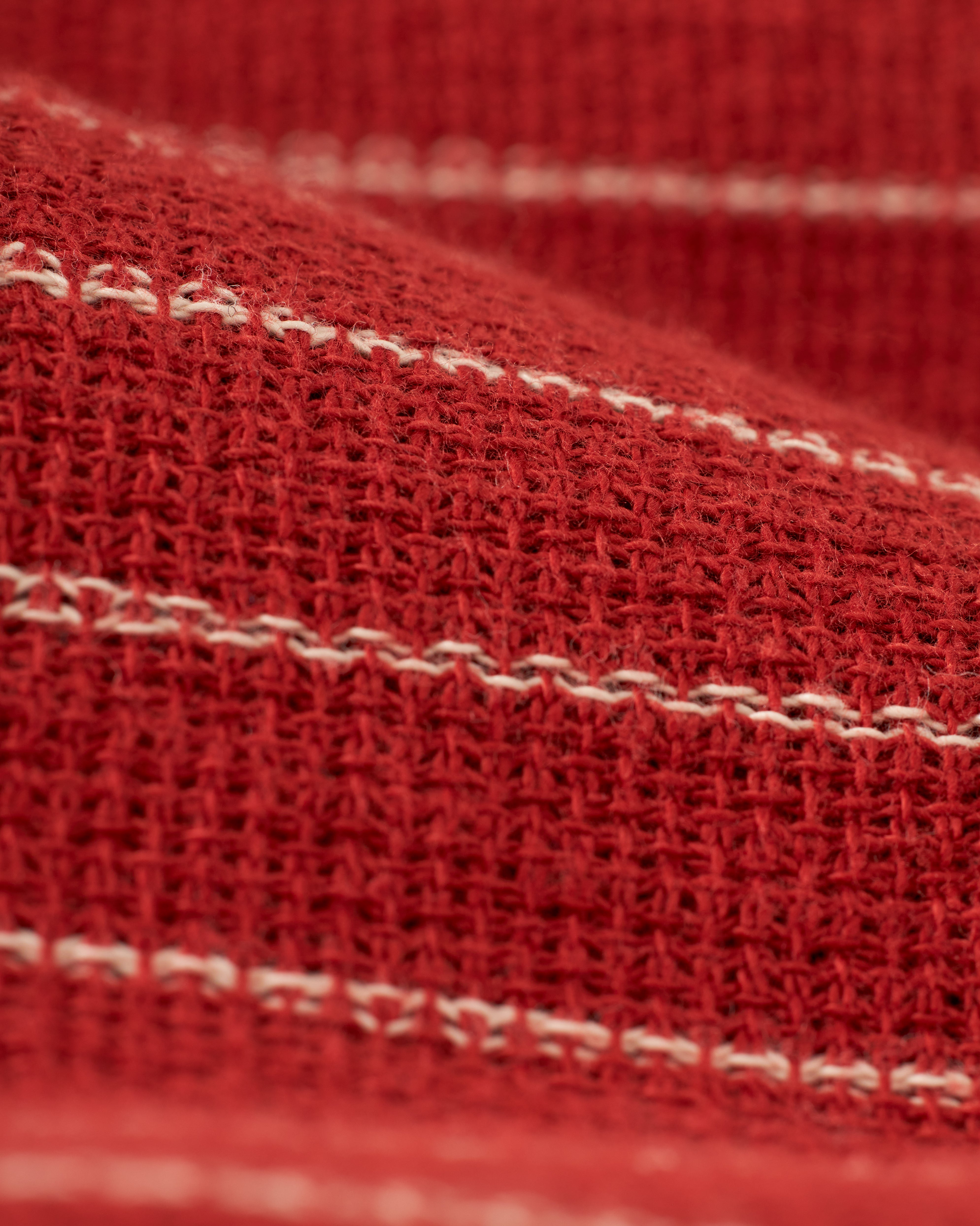 Close-up of a red textured fabric with white horizontal stripes, reminiscent of the intricate weave structure found in The Palma Shirt - Garam by Dandy Del Mar.