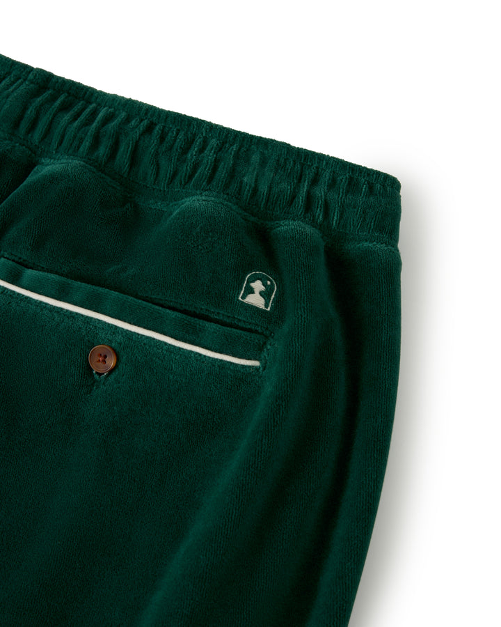 Close-up of The Rio Velour Short - Albero by Dandy Del Mar, showcasing a green velvet fabric with an elastic waistband, a back pocket with button closure, and a small embroidered logo above it.