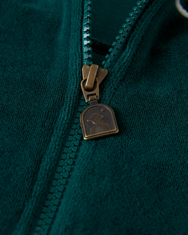 Close-up image of a green zipper on The Rio Velour Jacket - Albero by Dandy Del Mar, featuring a metallic zipper pull with a distinct embossed design.