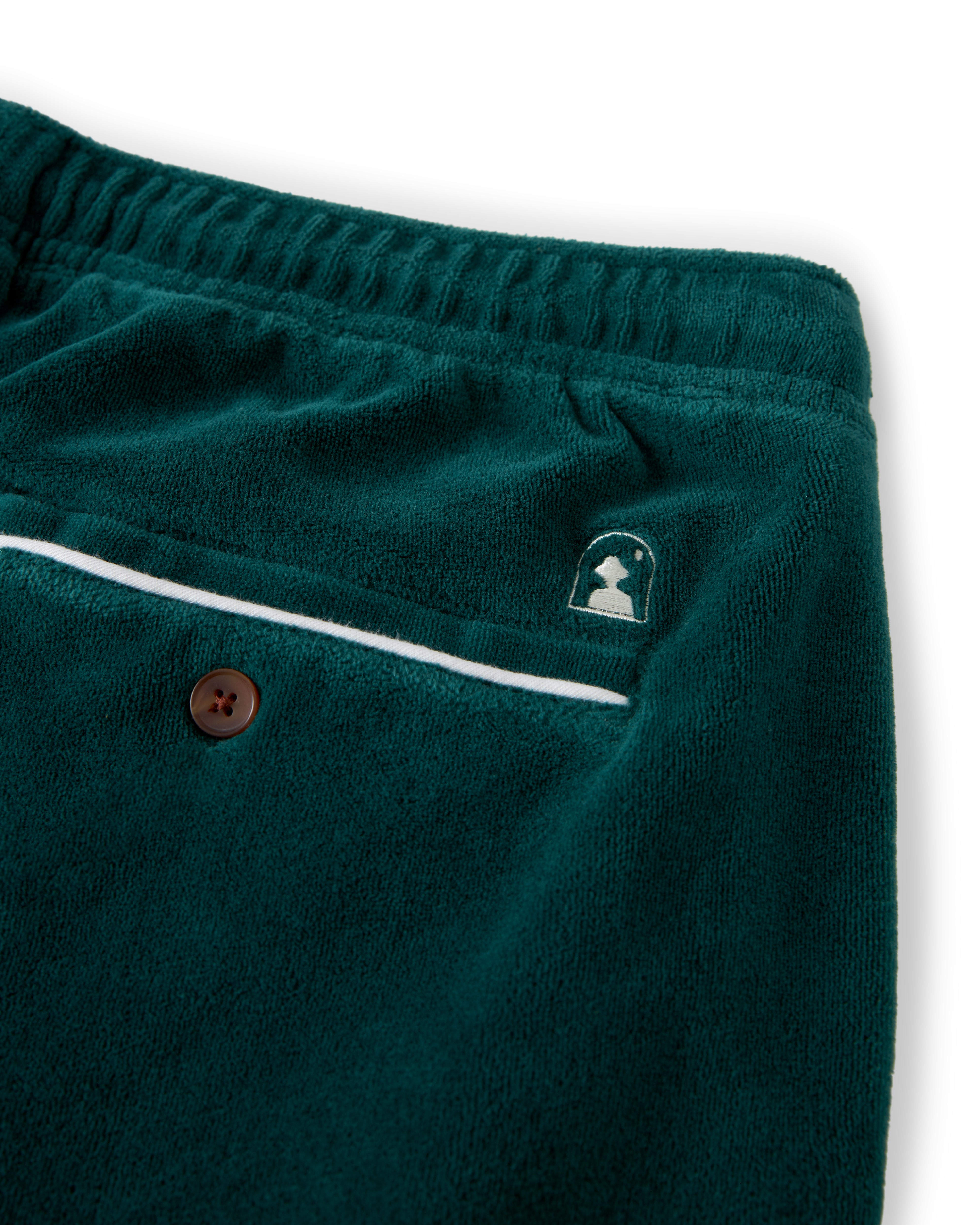 Close-up view of The Rio Velour Pant - Albero from Dandy Del Mar featuring an elastic waistband, brown button pocket, white piping, and a small embroidered logo. These relaxed fit pants blend athletic leisure with style for a comfortable yet trendy look.