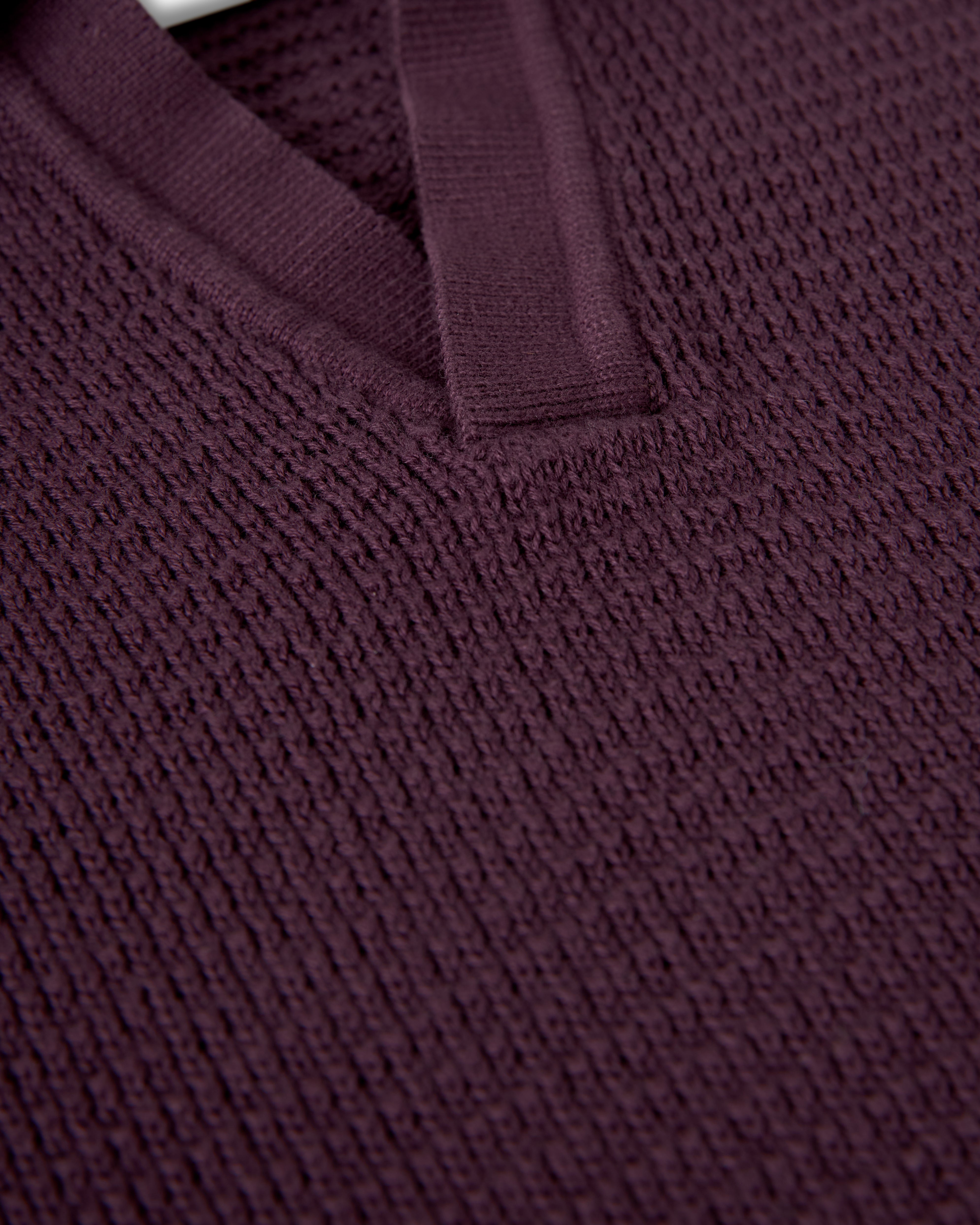 Close-up of The Sebastian Long Sleeve Polo in Amethyst by Dandy Del Mar, showcasing its dark purple sweater-knit cotton with a textured finish and V-neck collar.