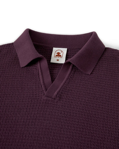 A close-up of The Sebastian LS Polo Shirt in Amethyst by Dandy Del Mar, size medium, highlights refined men's knitwear details with a textured maroon finish, collar, and visible brand tag.