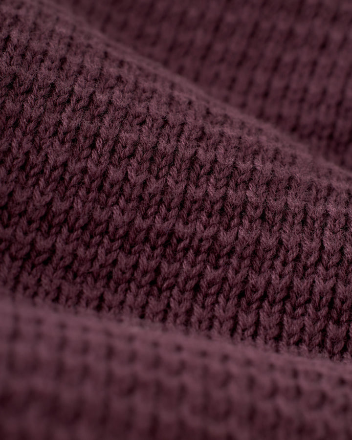 Close-up of the textured knit fabric in The Sebastian Long Sleeve - Amethyst by Dandy Del Mar, showcasing visible stitches that form a wavy pattern, reminiscent of rich maroon tones in this cozy cotton sweater.