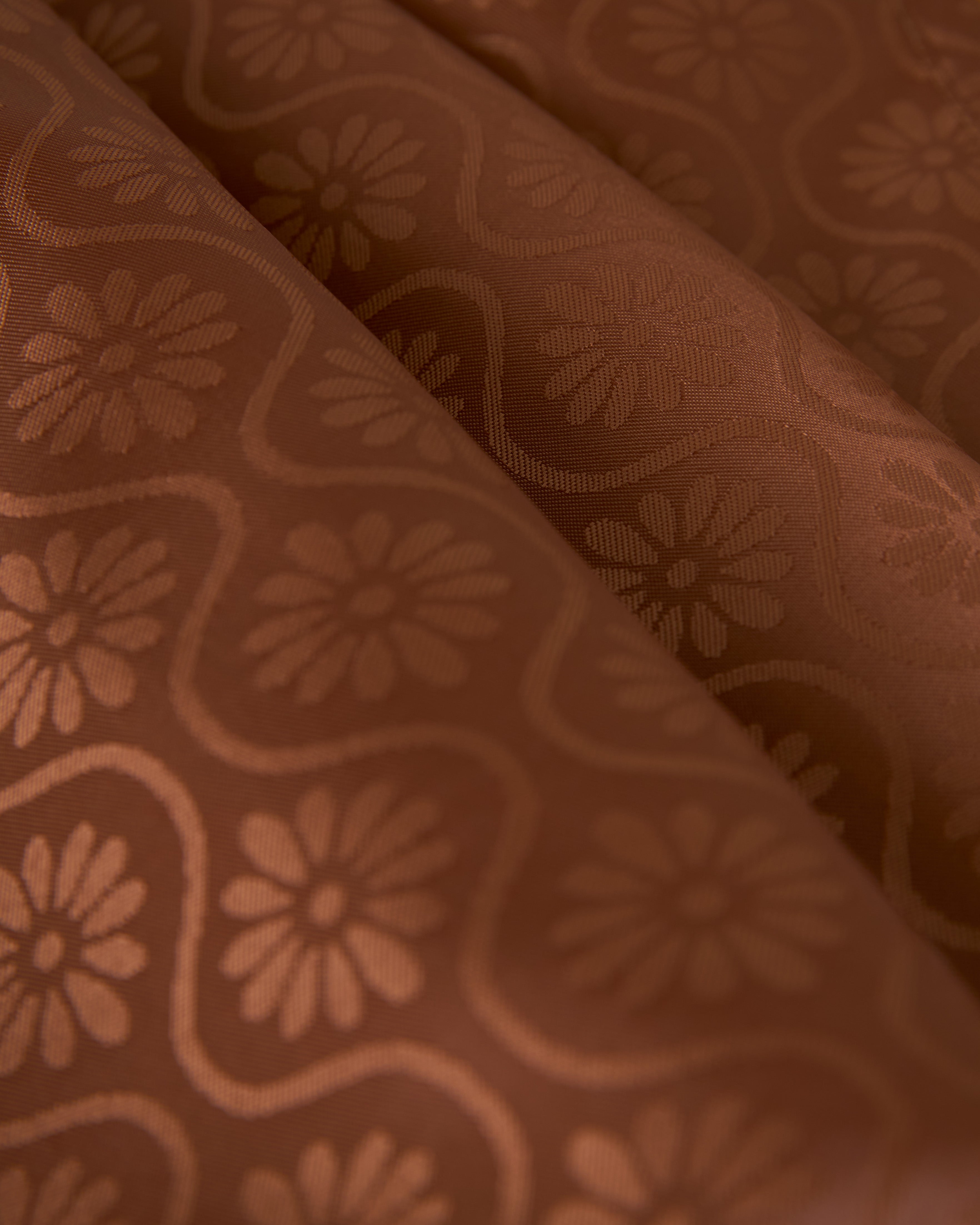 Close-up of brown fabric with a floral jacquard pattern, featuring a repetitive design of stylized flowers and curved lines, perfect for the lining of The Sicily Leather Jacket - Sable by Dandy Del Mar.