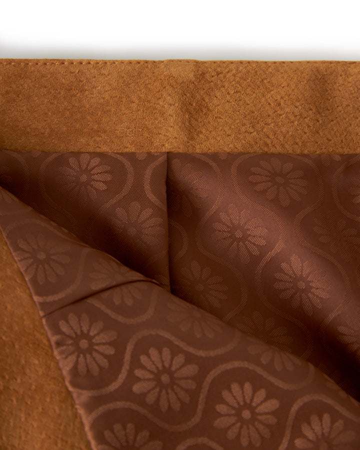 Close-up of a folded brown fabric with a flower pattern and a contrasting textured section above, reminiscent of the elegance found in Dandy Del Mar's The Sicily Leather Skirt - Sable.