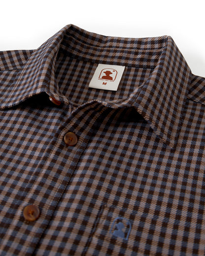 A close-up of the Tresco Shirt - Tierra Houndstooth by Dandy Del Mar, a brown and blue checkered woven collared button-up featuring a brand label marked "M." It exudes casual elegance perfect for any occasion.