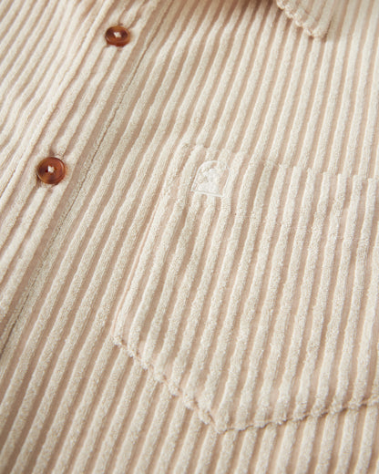 Close-up of a beige corduroy Tropez Jacquard Shirt - Scallop Stripe by Dandy Del Mar, featuring brown buttons and an embroidered logo on the chest pocket, reminiscent of the Côte d'Azur's effortless style.