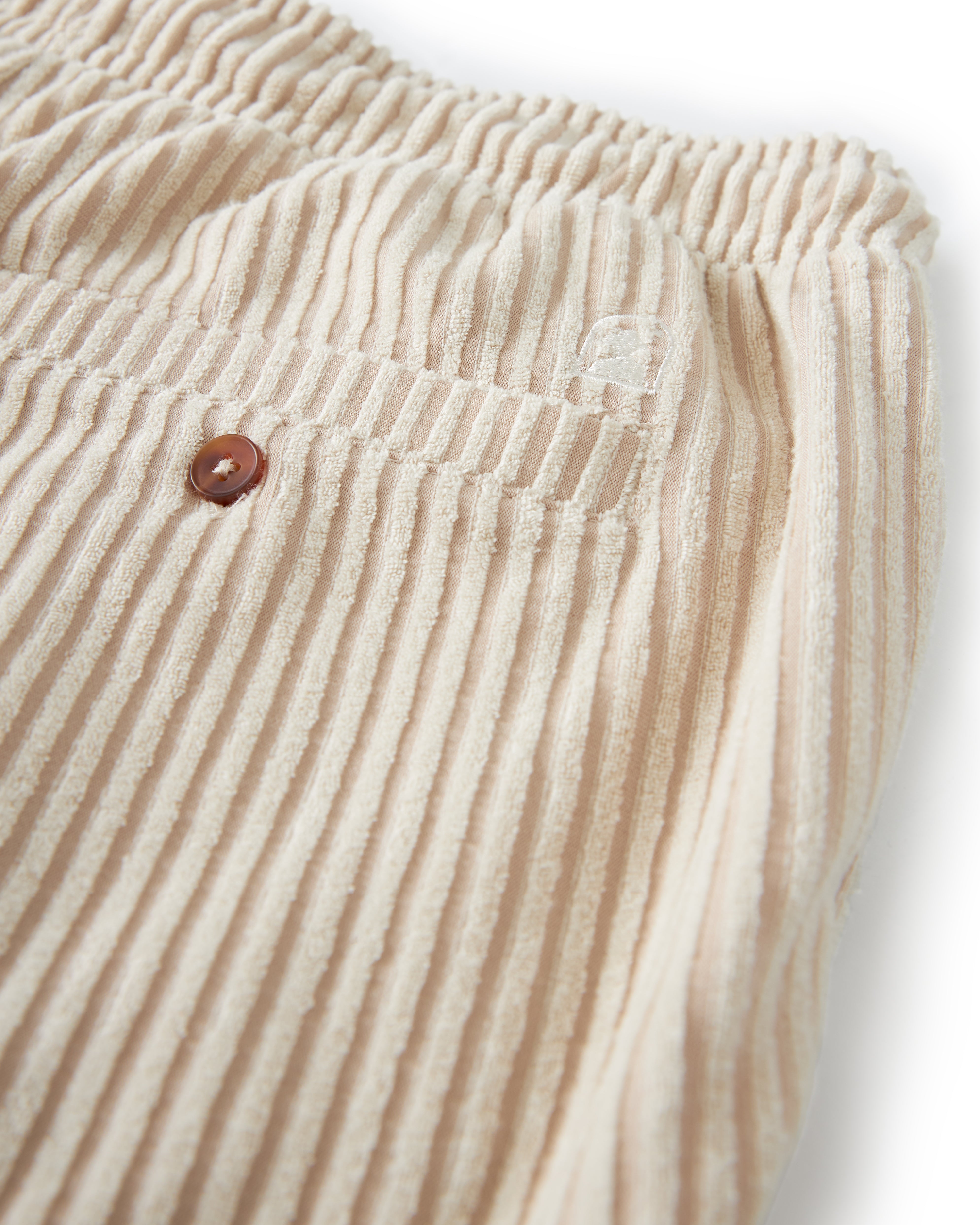 Close-up of The Tropez Jacquard Short - Scallop Stripe by Dandy Del Mar, showcasing its beige corduroy texture, elastic waistband, and a small pocket adorned with a brown button.