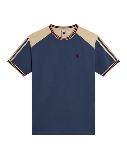 The Nassau Tee - Moontide by Dandy Del Mar is a soft cotton jersey tee with a navy body, beige raglan sleeves, striped trim on sleeves and collar, and an embroidered logo on the left chest.