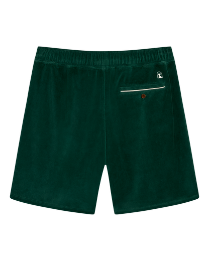 The Rio Velour Short - Albero by Dandy Del Mar features dark green velour fabric, an elastic waistband, a back zippered pocket, and a small logo patch above the pocket.