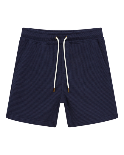 The Cannes Short - Luxe Navy by Dandy Del Mar features waffle knit fabric with a ribbed texture, two front pockets, and gold-tipped drawstrings, shown laid flat on a white background.