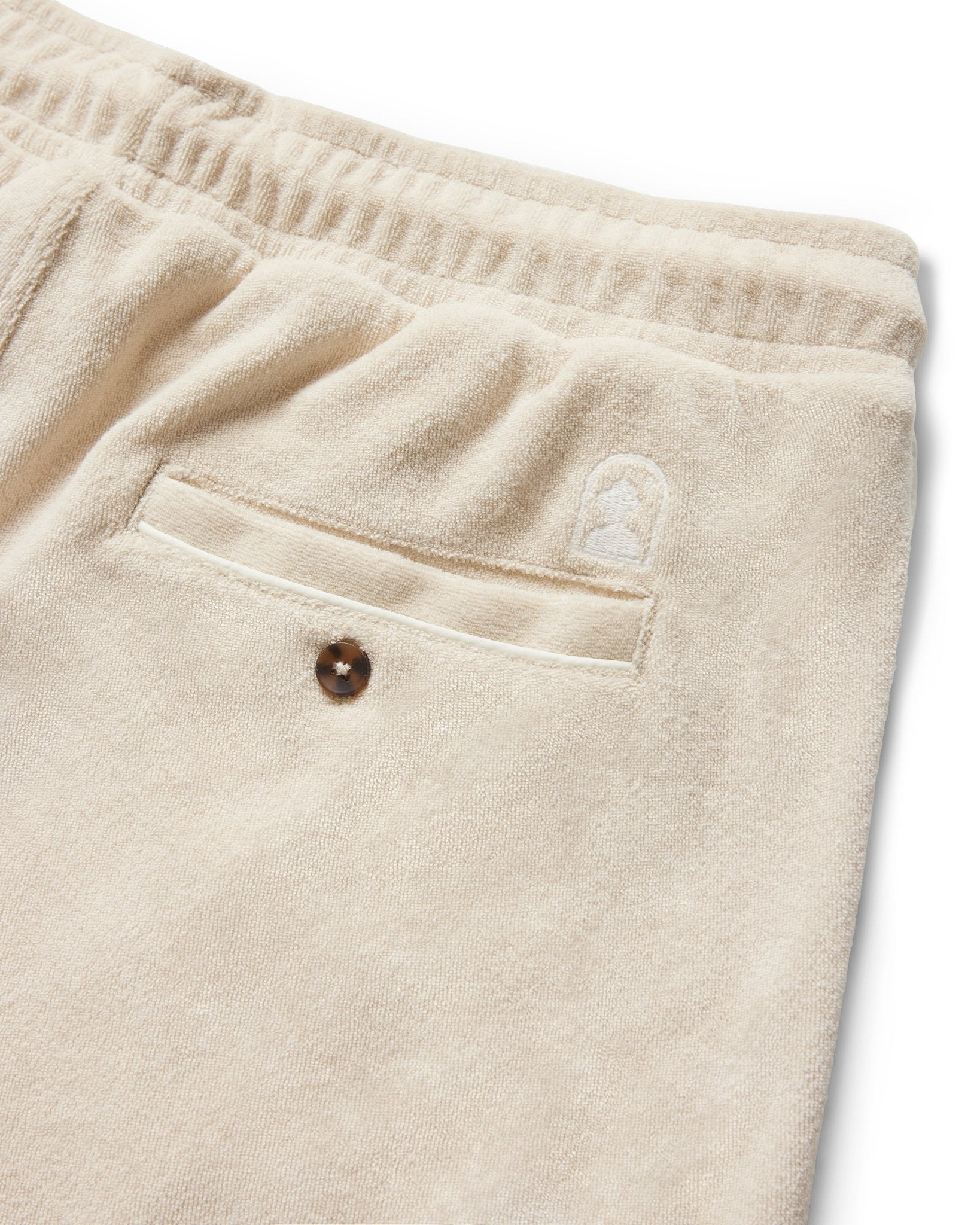 Close-up of Dandy Del Mar's The Gaucho Terry Cloth Shorts in Alabaster, featuring an elastic waistband, a back pocket with button, and a small embroidered logo above the pocket.