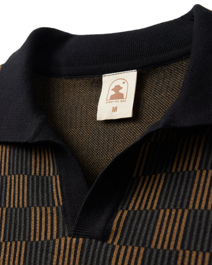 Close-up of a collared shirt with a brown and black checkered pattern. A label inside reads "Medium" with a logo featuring a silhouette of a person and the text "Dandy Del Mar." This piece pairs perfectly with The Sebastian Knit Polo - Onyx for an effortlessly stylish look.