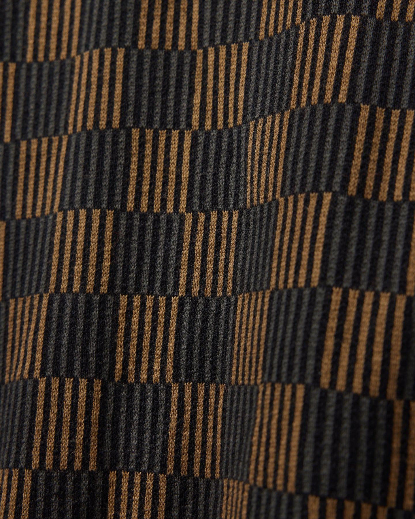 This close-up showcases The Sebastian Knit Polo in Onyx by Dandy Del Mar, featuring an Italian knit fabric with a checkered pattern of alternating black and brown stripes, creating an optical illusion.